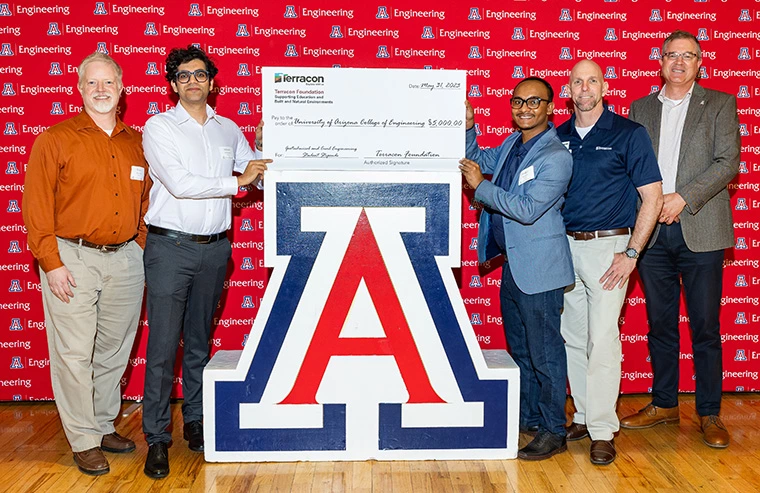 people standing next to UA logo, holding a check