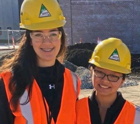 Two young women in yellow hardhats and orange safety vests