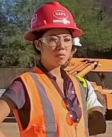 A woman wearing safety glasses, a red hard hat and an orange safety vest