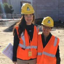 Lisette Flores and Rosa Juvera pose together in hard hats and reflective vests at a construction site