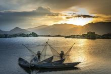 Two fishermen with nets standing in the Mekong River at sunset