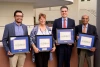 four people standing, holding awards