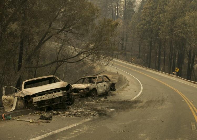 Two burned-out cars, pushed to the side of a two-lane paved road.