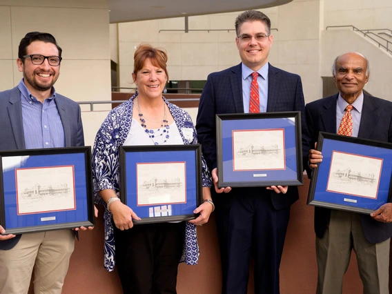 four people standing, holding awards