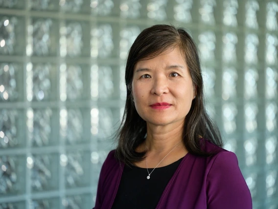 A woman with dark hair poses for a photo in front of a glass wall.