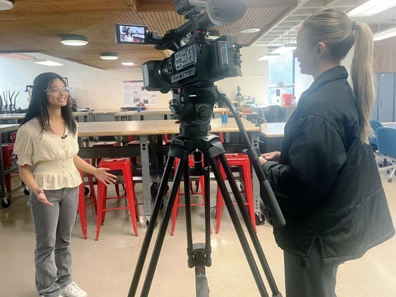 A young woman with brown hair is interviewed by a reporter.