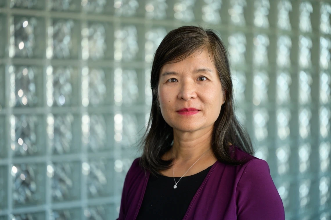 A woman with dark hair poses for a photo in front of a glass wall.