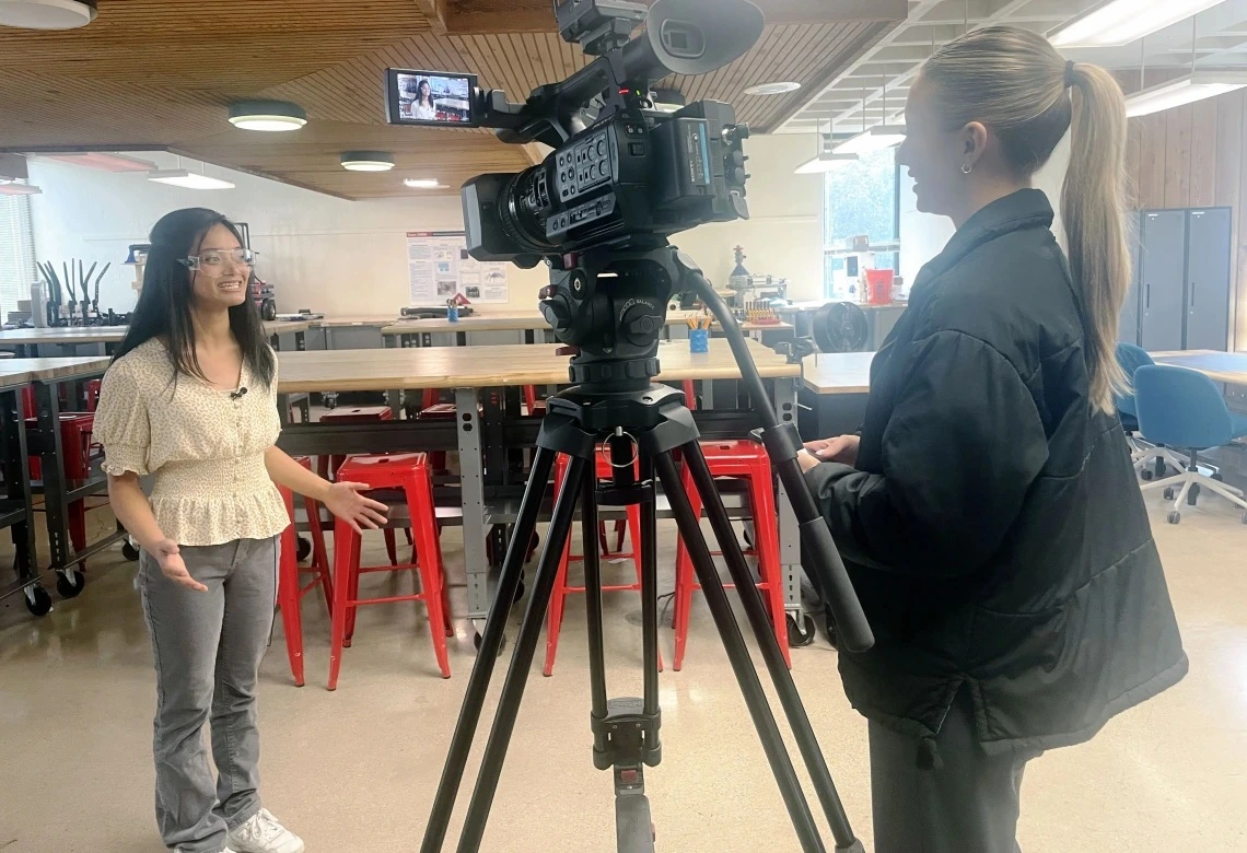 A young woman with brown hair is interviewed by a reporter.