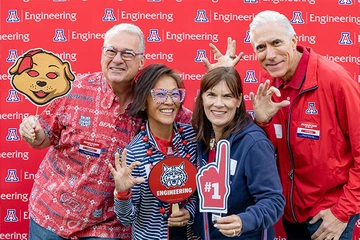 four people, smiling for camera, three holding university SWAG items