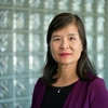 A woman with dark hair poses for a photo in front of a glass wall.
